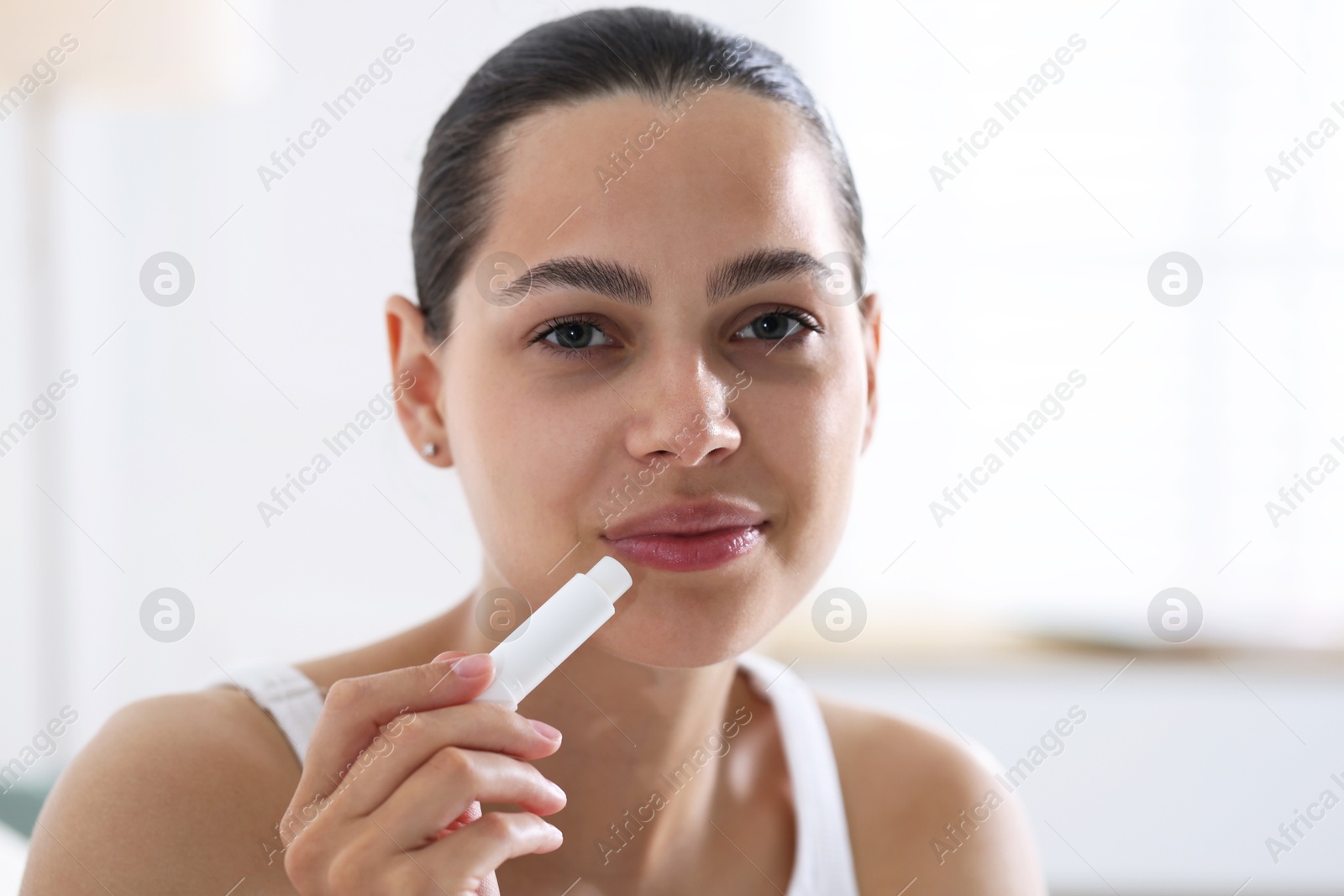 Young woman with lip balm at home Photo of Young woman with lip balm at home