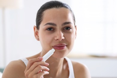 Photo of Young woman with lip balm at home