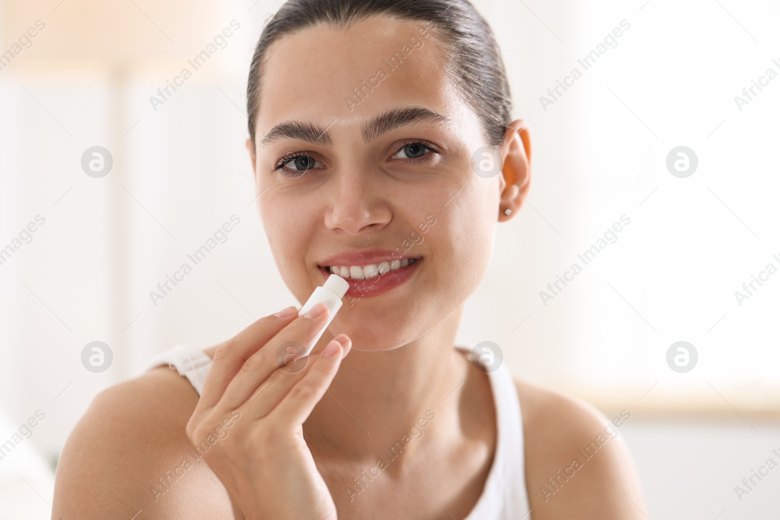 Young woman with lip balm at home Photo of Young woman with lip balm at home