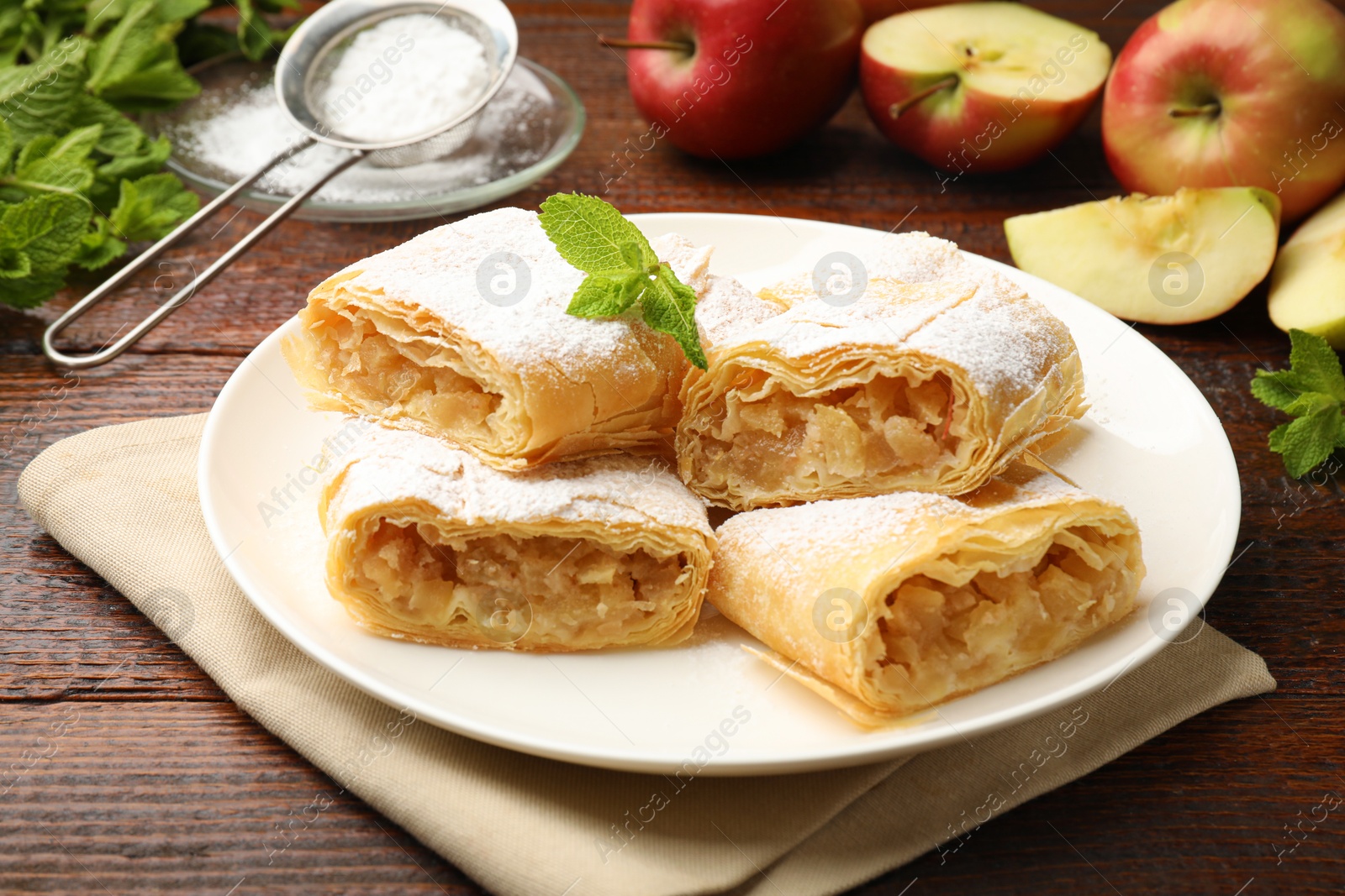 Pieces of tasty apple strudel with powdered sugar, mint and fruits on wooden table, closeup Photo of Pieces of tasty apple strudel with powdered sugar, mint and fruits on wooden table, closeup