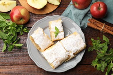 Photo of Pieces of tasty apple strudel with powdered sugar, mint and fruits on wooden table, flat lay