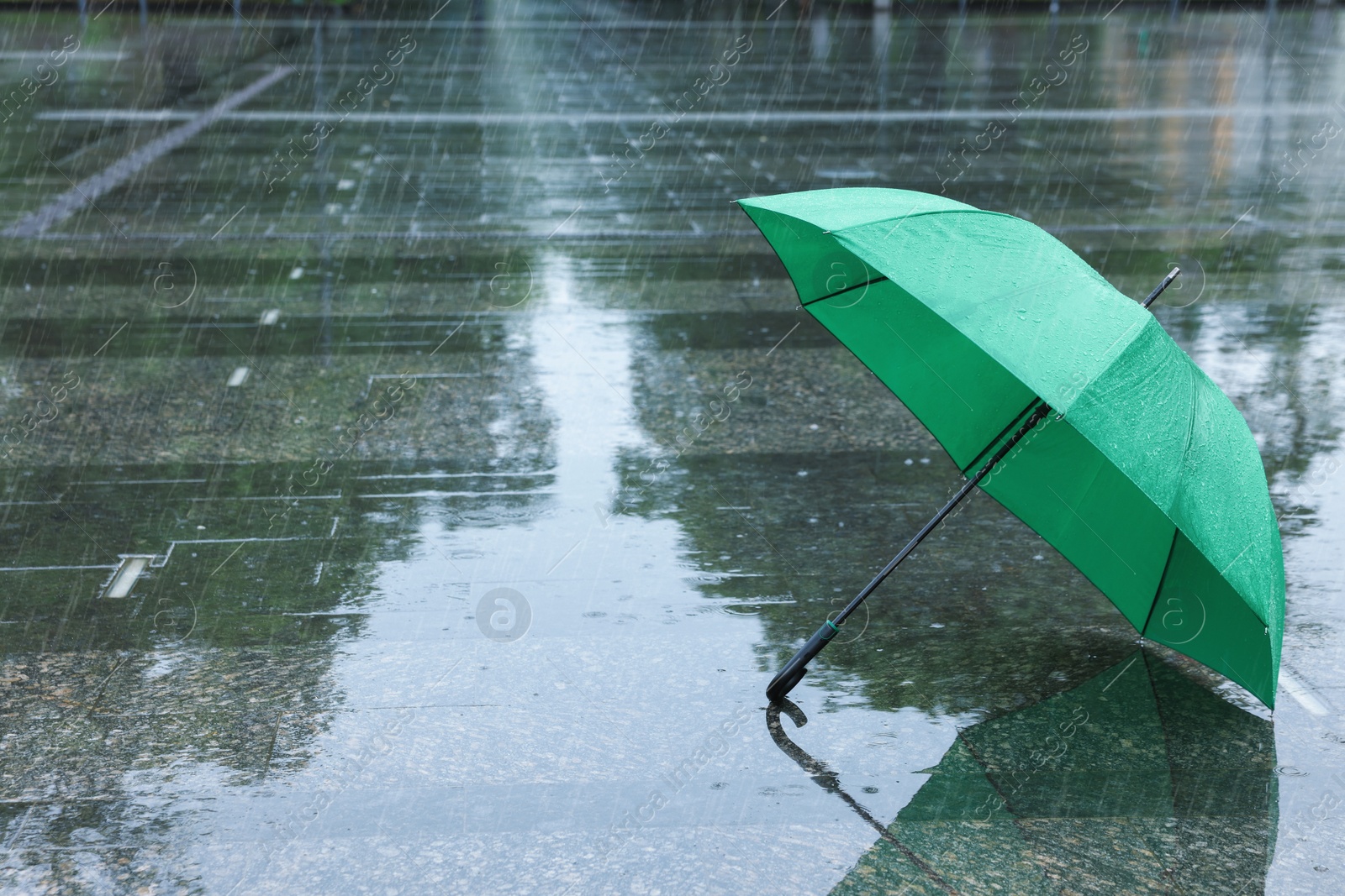 Green umbrella under heavy rain outdoors, space for text Photo of Green umbrella under heavy rain outdoors, space for text