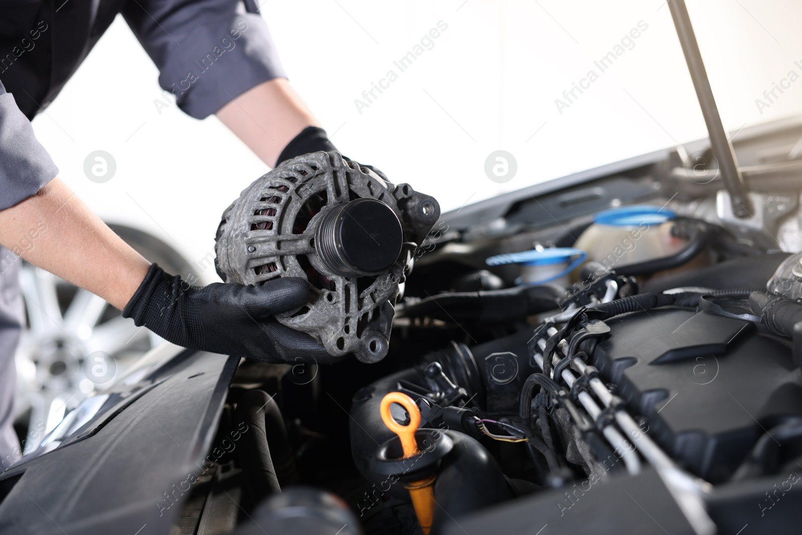 Auto part. Professional mechanic with alternator near open hood of car indoors, closeup Photo of Auto part. Professional mechanic with alternator near open hood of car indoors, closeup