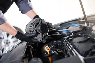 Photo of Auto part. Professional mechanic with alternator near open hood of car indoors, closeup