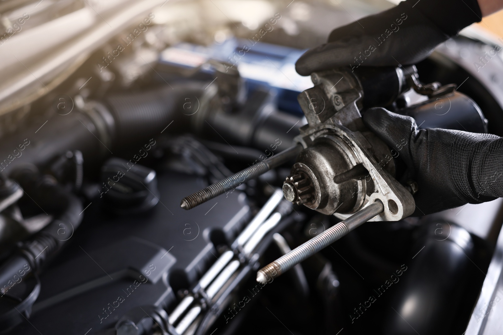 Auto part. Professional mechanic with starter motor near open hood of car indoors, closeup Photo of Auto part. Professional mechanic with starter motor near open hood of car indoors, closeup