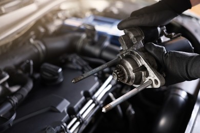 Photo of Auto part. Professional mechanic with starter motor near open hood of car indoors, closeup