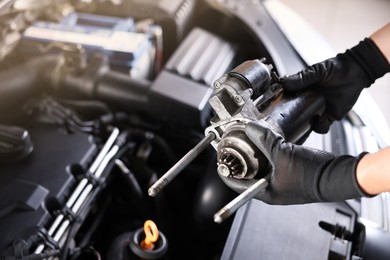Photo of Auto part. Professional mechanic with starter motor near open hood of car indoors, closeup