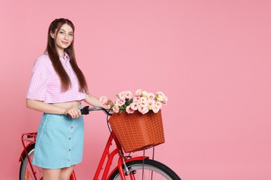Photo of Beautiful woman and bicycle with basket of flowers against pink background. Space for text