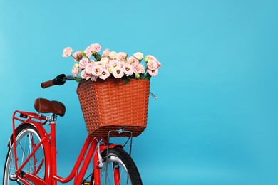 Photo of Bicycle with basket of beautiful flowers on light blue background. Space for text