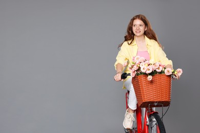 Photo of Smiling teenage girl riding bicycle with basket of flowers against grey background. Space for text
