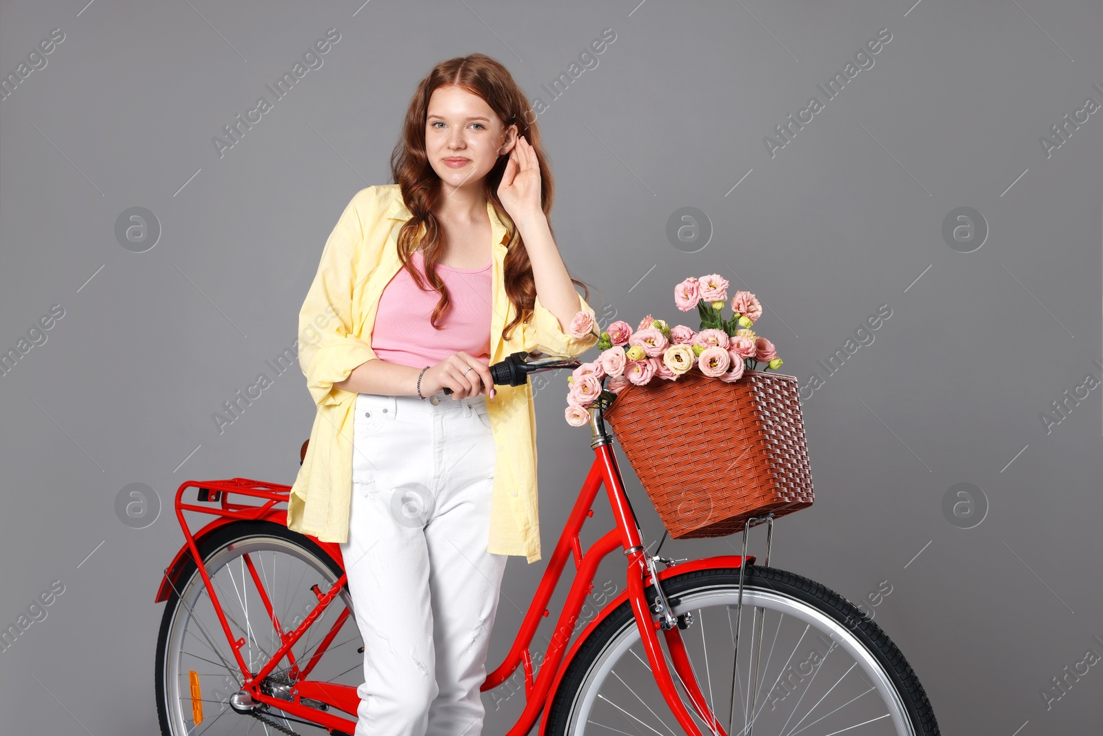 Beautiful teenage girl and bicycle with basket of flowers against grey background Photo of Beautiful teenage girl and bicycle with basket of flowers against grey background