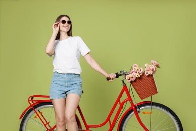 Photo of Smiling woman in sunglasses and bicycle with basket of flowers on green background