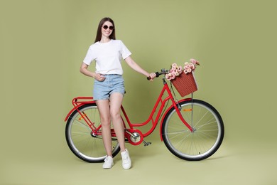 Photo of Smiling woman in sunglasses and bicycle with basket of flowers on green background