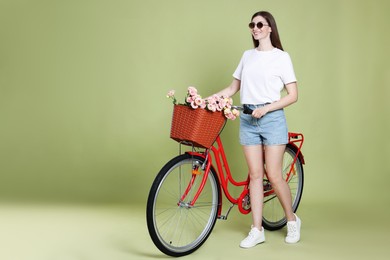 Photo of Smiling woman in sunglasses and bicycle with basket of flowers on green background. Space for text