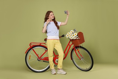 Photo of Smiling teenage girl taking selfie and bicycle with basket of flowers against green background