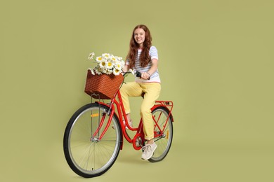 Photo of Smiling teenage girl riding bicycle with basket of flowers against green background