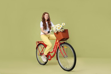 Photo of Smiling teenage girl riding bicycle with basket of flowers against green background