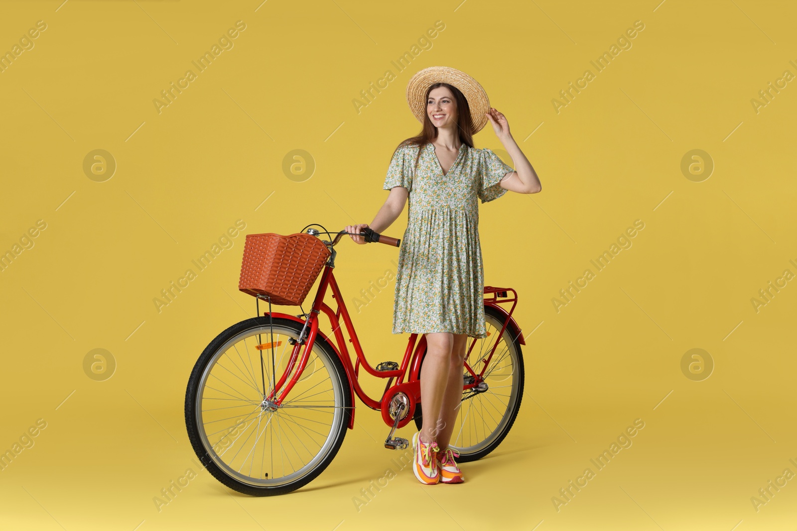 Smiling woman in hat and bicycle with basket on yellow background Photo of Smiling woman in hat and bicycle with basket on yellow background