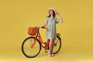 Photo of Smiling woman in hat and bicycle with basket on yellow background