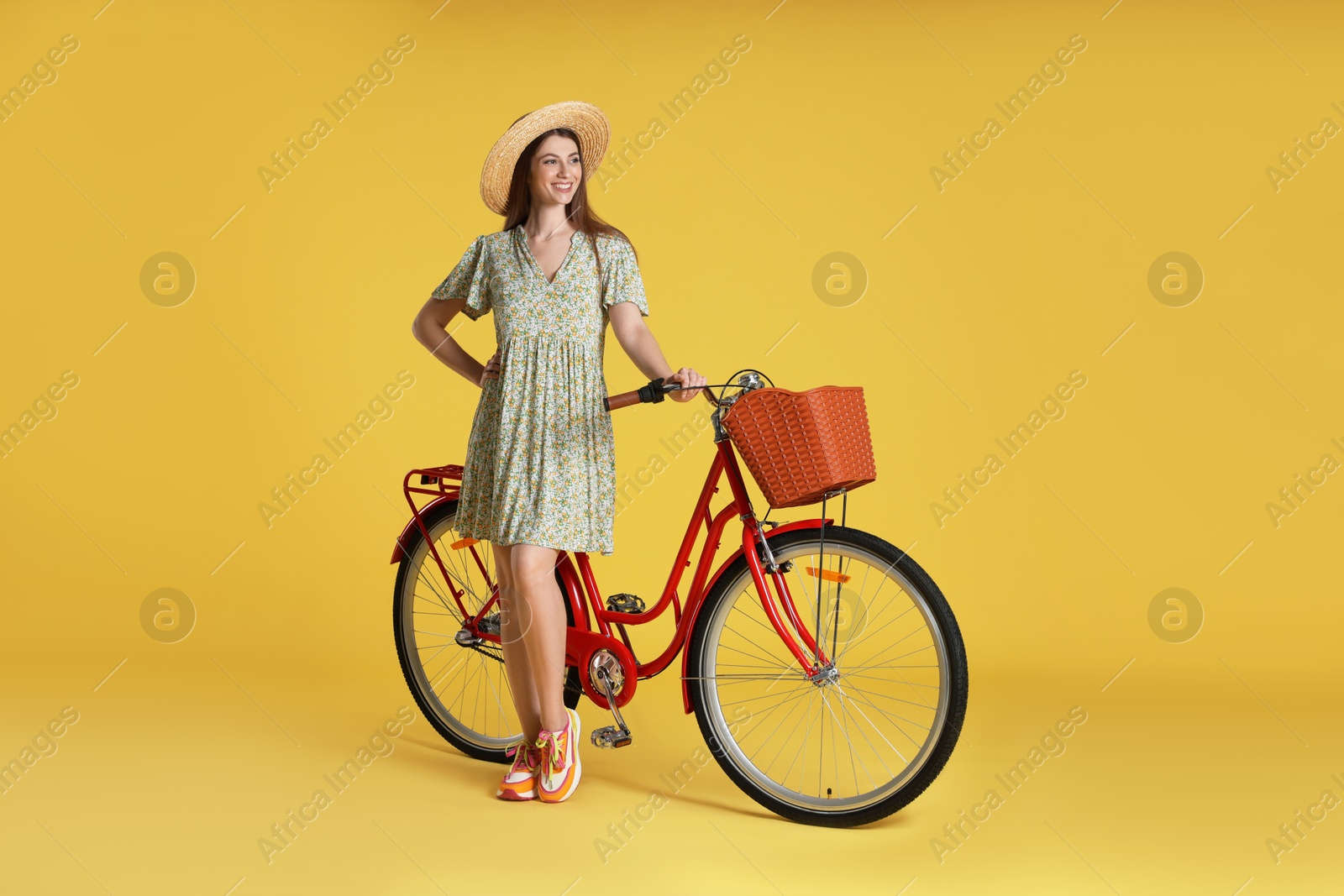 Photo of Smiling woman in hat and bicycle with basket on yellow background