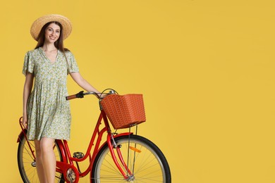 Photo of Smiling woman in hat and bicycle with basket on yellow background. Space for text
