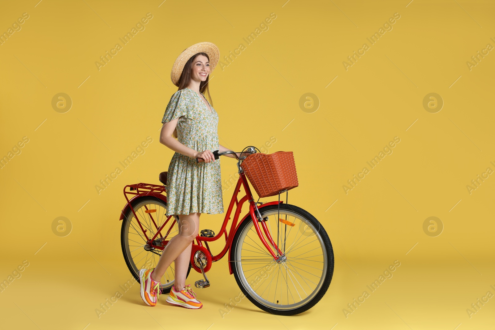 Photo of Smiling woman in hat and bicycle with basket on yellow background