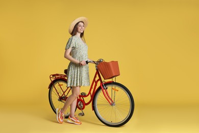 Photo of Smiling woman in hat and bicycle with basket on yellow background