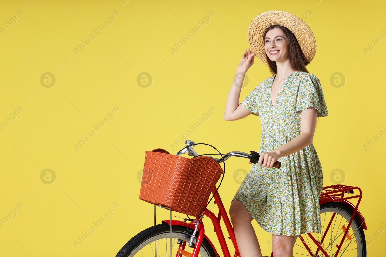 Photo of Smiling woman in hat posing on bicycle with basket against light green background. Space for text