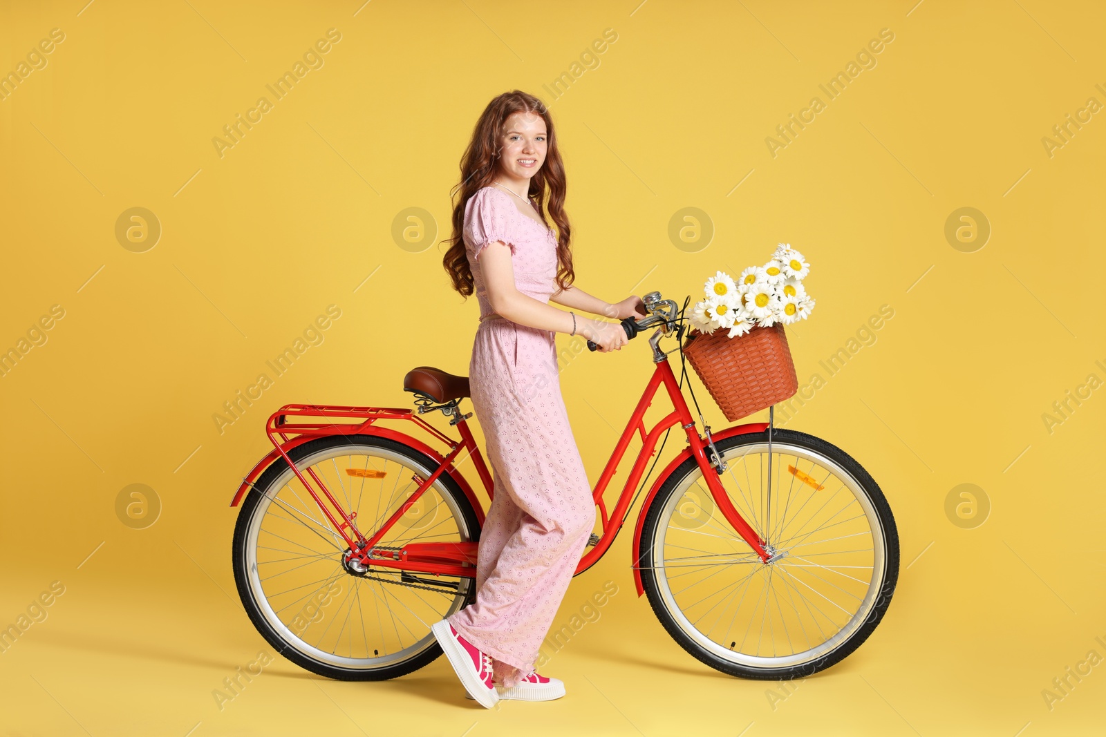 Photo of Smiling teenage girl and bicycle with basket of flowers against yellow background