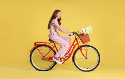 Photo of Smiling teenage girl riding bicycle with basket of flowers against yellow background