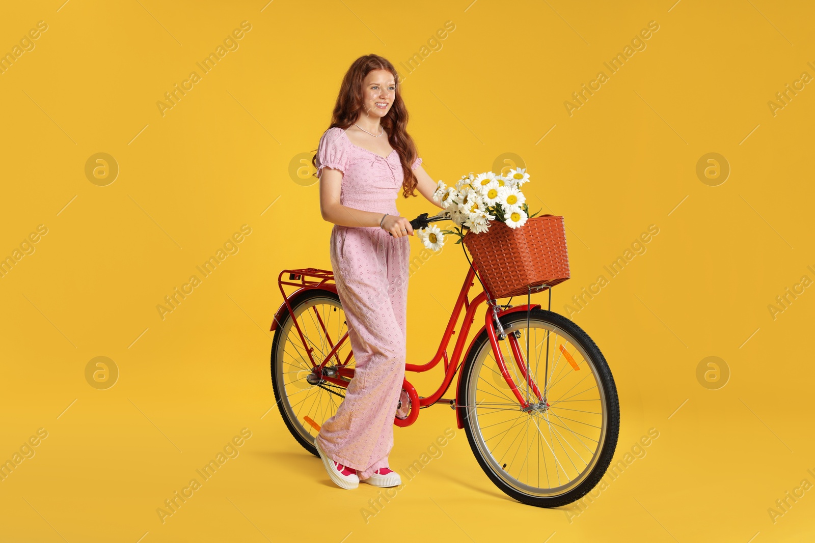 Photo of Smiling teenage girl and bicycle with basket of flowers against yellow background