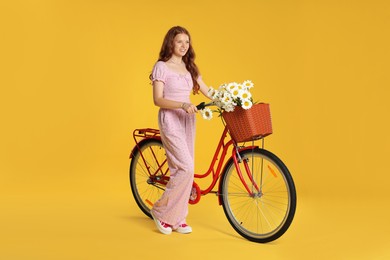 Photo of Smiling teenage girl and bicycle with basket of flowers against yellow background