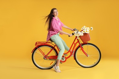 Photo of Smiling woman riding bicycle with basket of flowers against yellow background