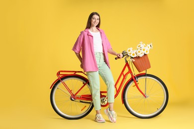 Photo of Smiling woman and bicycle with basket of flowers against yellow background