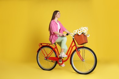 Photo of Smiling woman riding bicycle with basket of flowers against yellow background