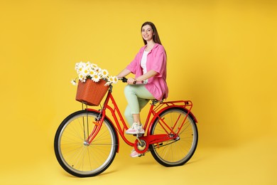 Photo of Smiling woman riding bicycle with basket of flowers against yellow background