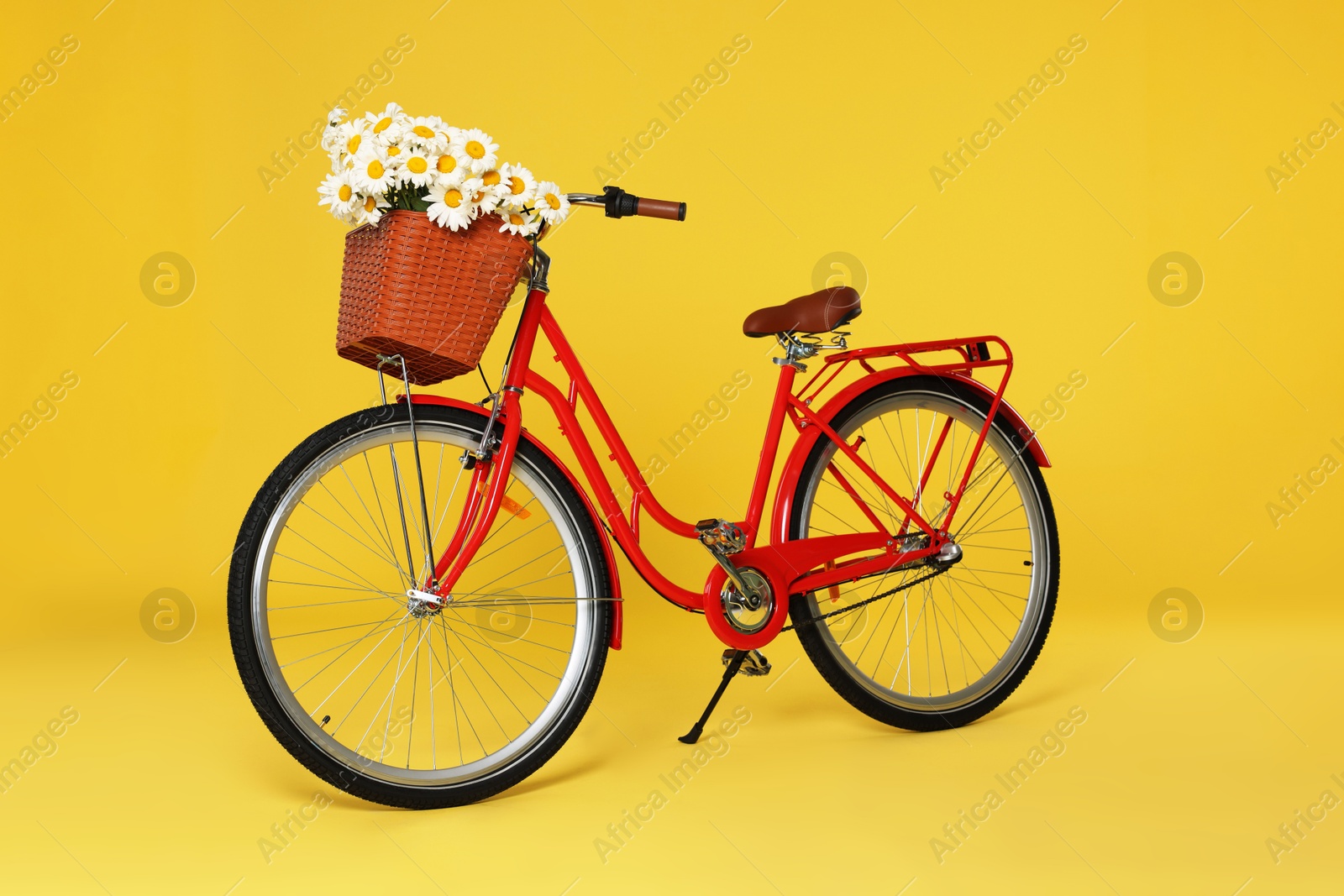 Bicycle with basket of beautiful flowers on yellow background Photo of Bicycle with basket of beautiful flowers on yellow background