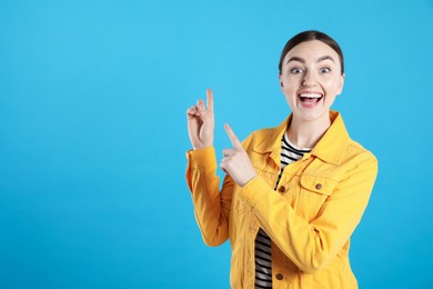 Photo of Surprised woman pointing at something on light blue background, space for text