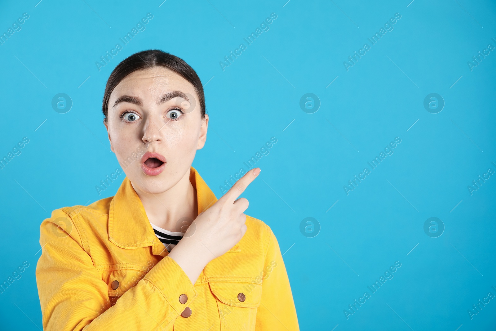 Photo of Surprised woman pointing at something on light blue background, space for text