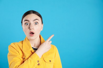 Photo of Surprised woman pointing at something on light blue background, space for text