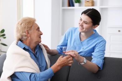 Photo of Nurse giving glass of water to senior woman indoors. Home health care service