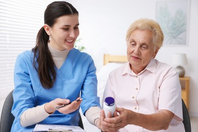 Photo of Nurse giving pills to senior woman indoors. Home health care service