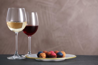 Photo of Delicious truffle bonbons and wine on black table against grey background. Space for text