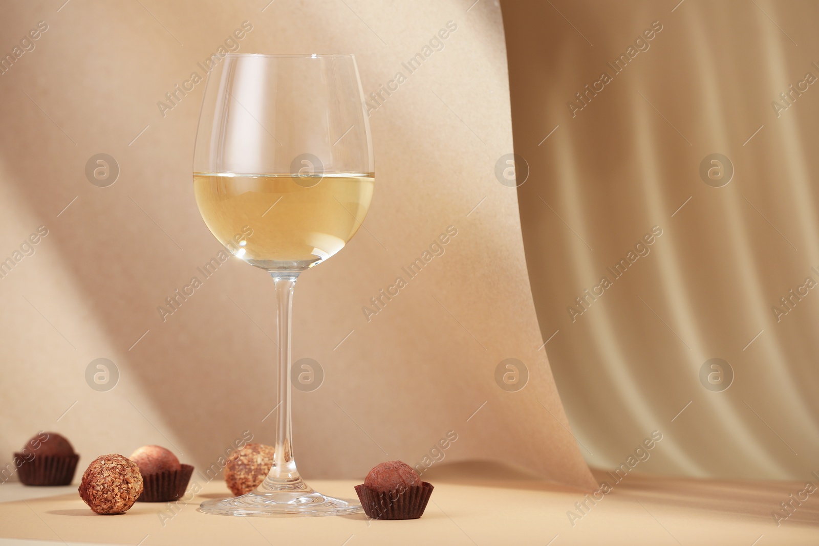 Delicious truffle bonbons and wine on beige background. Space for text Photo of Delicious truffle bonbons and wine on beige background. Space for text