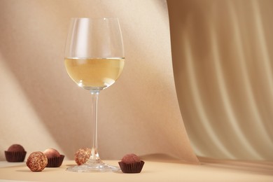 Photo of Delicious truffle bonbons and wine on beige background. Space for text