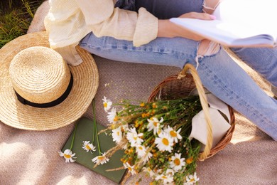 Photo of Woman with bouquet of wildflowers reading book on blanket in meadow, closeup