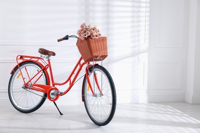 Photo of Bicycle with basket of beautiful flowers near white wall indoors. Space for text