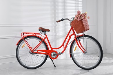 Photo of Bicycle with basket of beautiful flowers near white wall indoors
