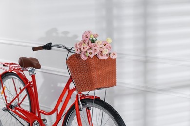 Photo of Bicycle with basket of beautiful flowers near white wall indoors, closeup. Space for text