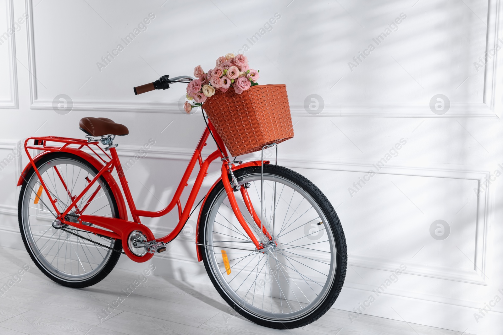 Bicycle with basket of beautiful flowers near white wall indoors. Space for text Photo of Bicycle with basket of beautiful flowers near white wall indoors. Space for text